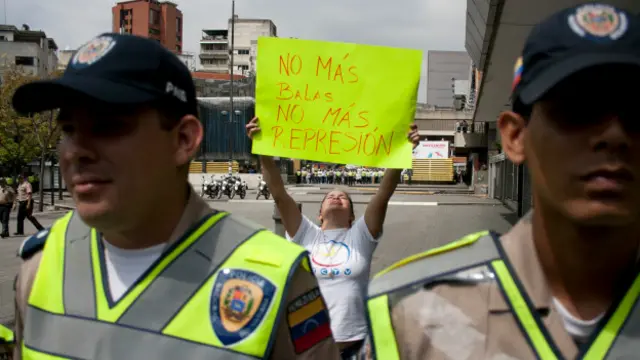 Policías venezolano delante de un cartel de protesta