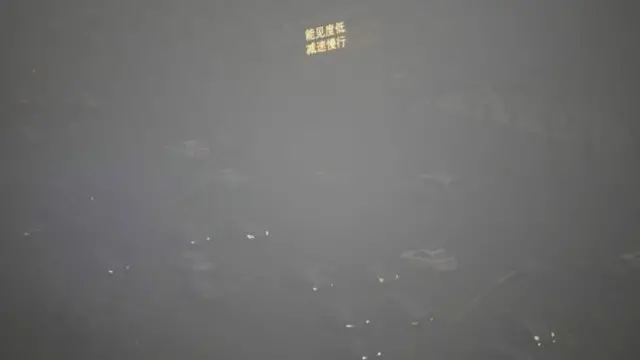 السيارات لا تكاد تظهر بسبب تلوث الهواء وفي الأعلى إشارة ضوئية تدعو إلى السير ببطء بسبب ضعف الرؤية