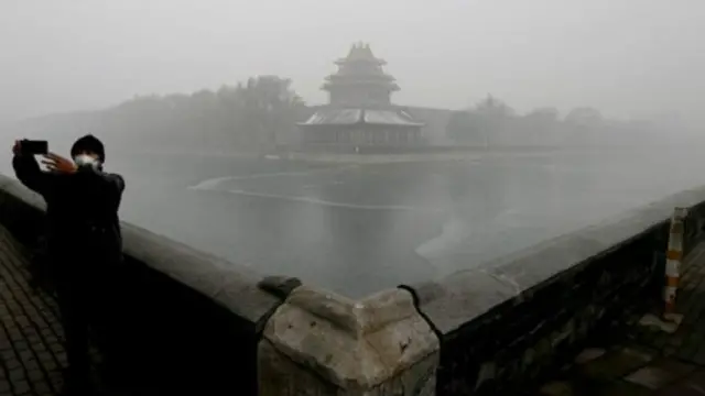 أحد السياح يلتقط صورة لنفسه وسط الضباب الدخاني وقد غطى أنفه بكمامة