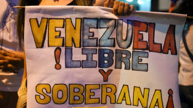 Una joven con un poster sobre Venezuela que lee: "libre y soberana"