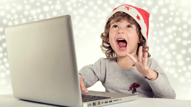 Un niño con gorro de navidad feliz frente a una laptop