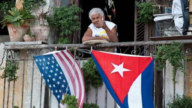 Hombre asomado en una ventana de la que cuelgan las banderas de EE.UU. y Cuba