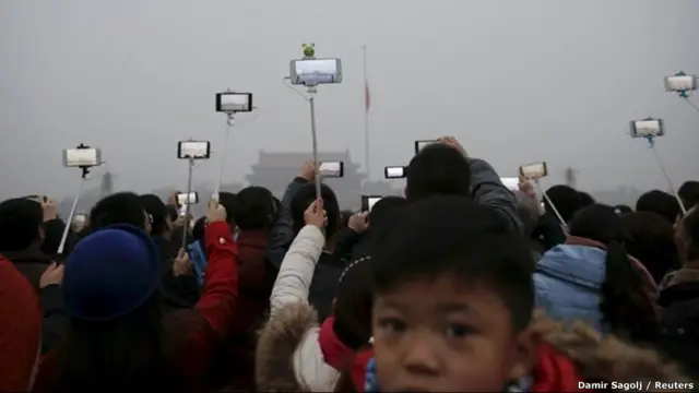 А це - церемонія підняття прапору на площі Тяньаньмень у Пекіні. Люди знімають подію на телефон, але їм заважає смог. У грудні 2015 року у китайській столиці на три днів вперше в історії оголосили "червоний рівень" загрози через надмірну забрудненість повітря.