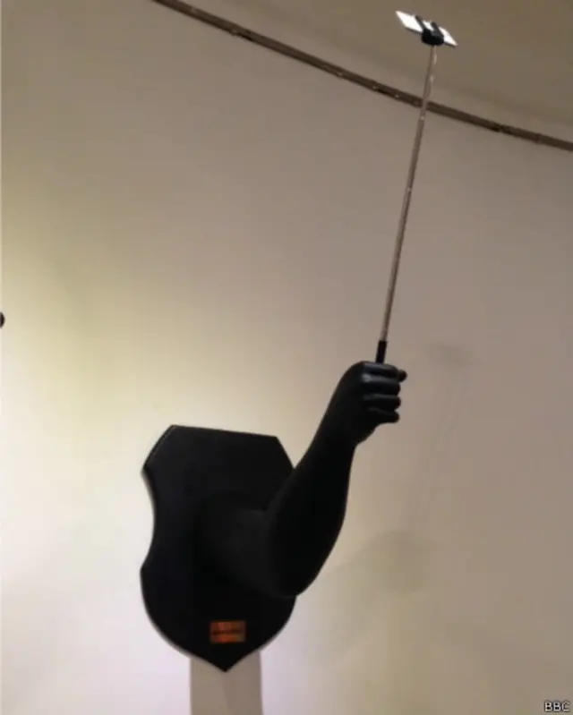 Tangan hitam yang memegang tongkat narsis alias tongsis.