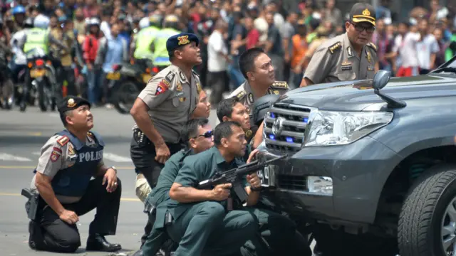 Kerumunan masyarakat menonton saat polisi mengambil posisi di belakang mobil. 