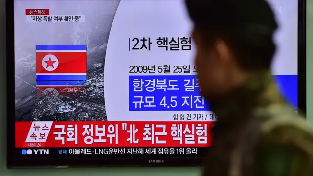 韩国首尔火车站一名士兵走过播放朝鲜核试验消息的电视屏幕（6/1/2016）