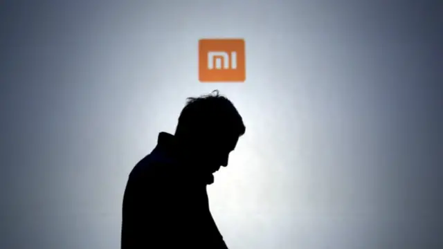 Силуэт мужчины, использующего смартфон на фоне логотипа Xiaomi