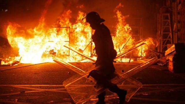 香港旺角衝突一名防暴警察在示威者焚燒的雜物堆前走過（9/2/2016）