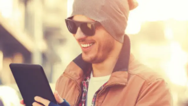 Un hombre con gafas de sol y gorro revisa su tableta