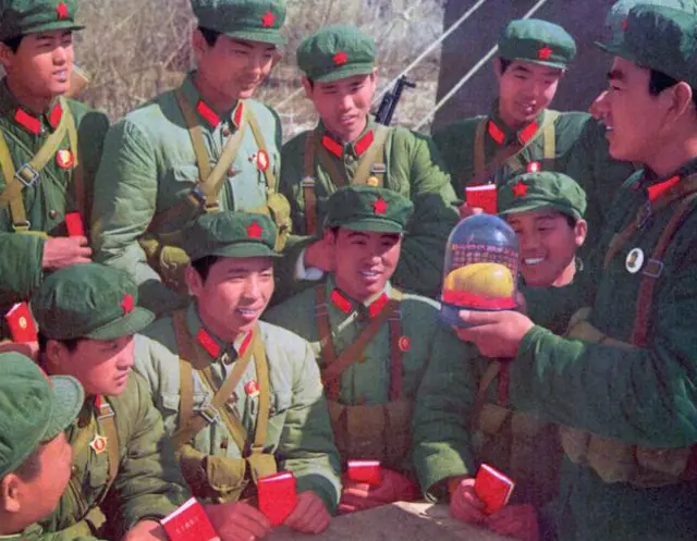 Miembros del Ejército de Liberación Popular observando una réplica de un mango protegida con una campana de vidrio.