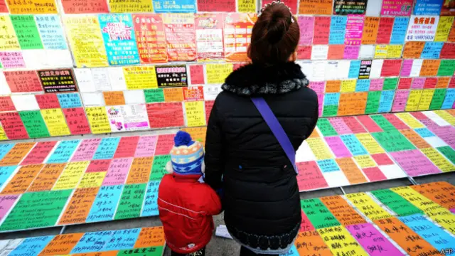 Mujer en China con un niño mira anuncios de trabajo