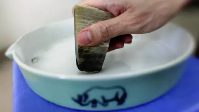 越南河内某商店内一名男士示范如何将犀牛角片磨粉(资料图片)