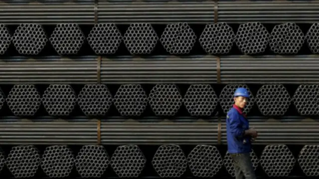 中国河北省一名钢铁工人在堆积的钢材前走过