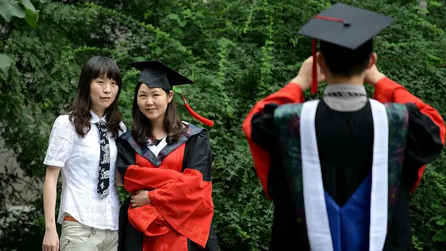 Un joven vestido con toga y birrete toma una foto a otra graduanda china.