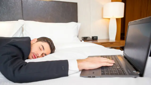 Una persona dormida sobre una laptop en una habitación de hotel