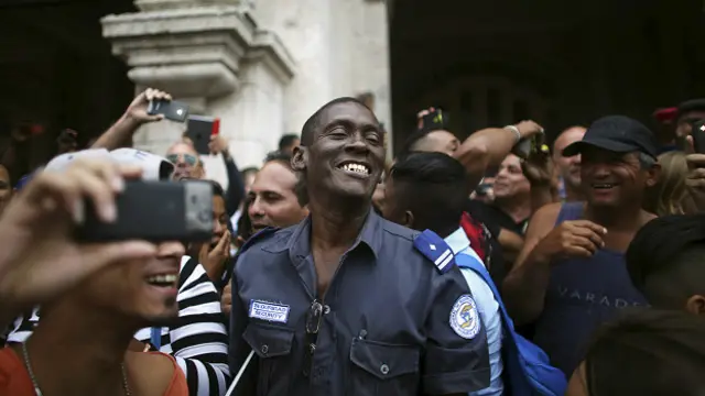 Un policía del gobierno cubano sonríe junto a la multitud mientras esperaban que el presidente Obama pasara por Centro Habana