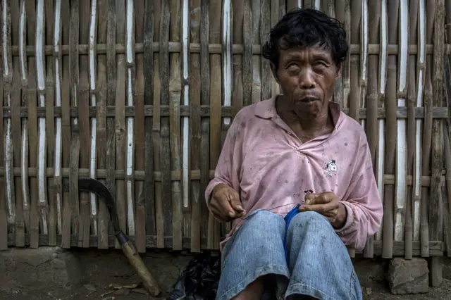 Bosrot, 55, menderita Down Syndrome, duduk di depan rumahnya di Desa Krebet.