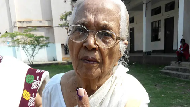 असम की 91 साल की मतदाता सरस्वती देवी मतदान के बाद स्याही लगी उंगली दिखाती हुई.