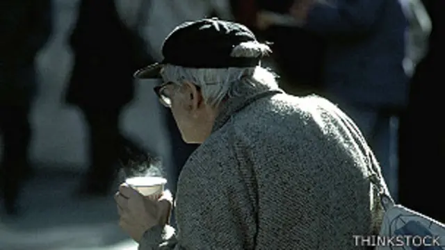 Persona mayor caminando en la calle con una bebida en la mano