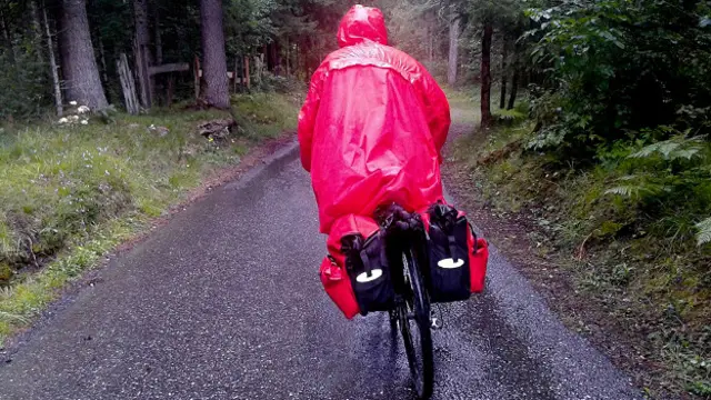 Велопидедист в розовом плаще на лесной дороге