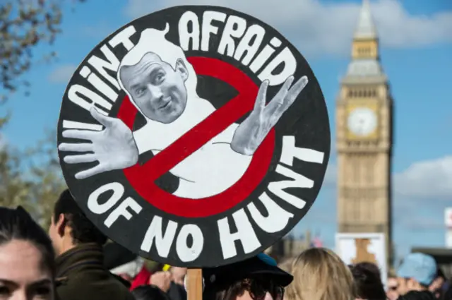 Младший доктор с плакатом в руках, изображающим министра здравоохранения Джереми Ханта