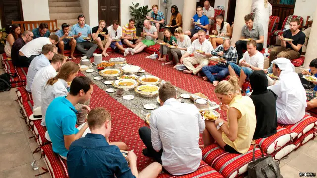 Para turis mengelilingi hidangan tradisional Emirat.