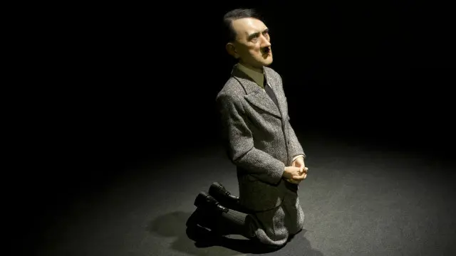 希特勒双膝跪地，两手互握，状似祈祷，塑像由蜡和树脂制成。