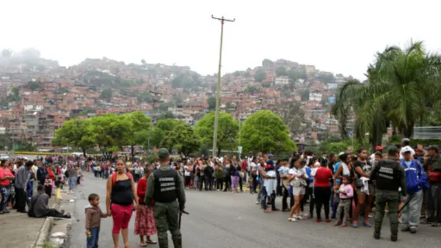 عضو گارد ملی هنگام حفظ نظم در صف دریافت جیره مواد غذایی در برابر یک سوپر مارکت