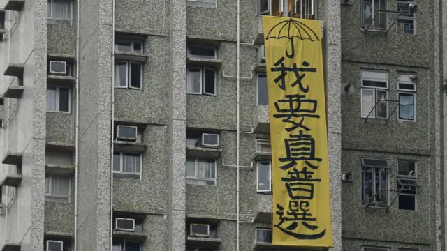 張德江訪問安老中心時，旁邊的居民樓上掛出抗議標語。