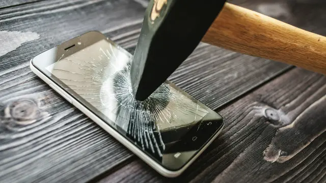 Una persona dándole un martillazo a un teléfono