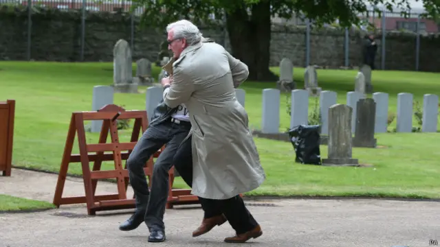 维克尔斯（着风衣者）阻止抗议者莫菲冲上讲台