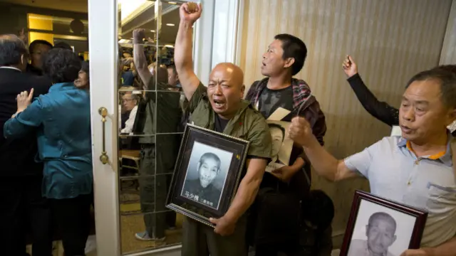 劳工遗属在新闻发布会上手持受害者遗像高叫口号