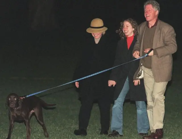 Hillary, Chelsea y Bill Clinton sonrientes con un perro