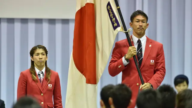 日本代表團首席選手吉田沙保裏（左）與持棋手右代啟佑在東京的送行儀式上展示日本國旗（3/7/2016）