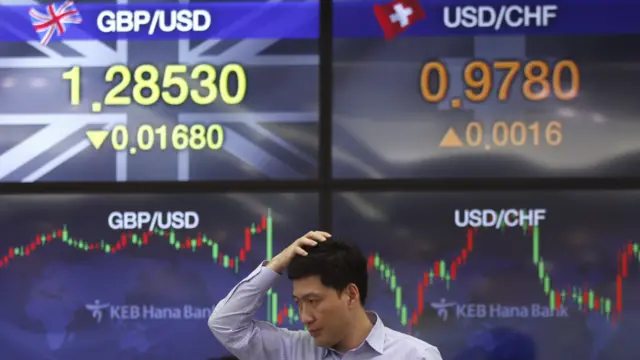 韩国一名货币交易员7月6日行经挂有外币汇率的街头。