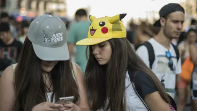 2016年7月28日，马德里的一个女孩带着皮卡丘的帽子看朋友在使用《Pokémon GO》应用。(图片来源：Getty Images)