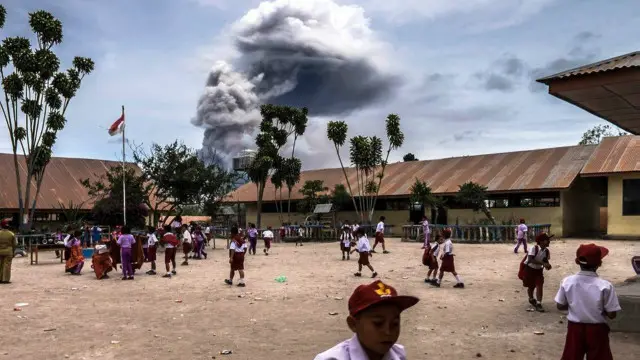 أطفال في مدرسة في جزيرة سومطرة يلعبون في فناء المدرسة بقرية غاجا تزامنا مع إطلاق جبل سينابونغ دفعات من الرماد البركاني في الهواء على مقربة منهم. وثار بركان سينابونغ عام 2010 بعد 400 سنة من الخمول، لكنه عاد لينشط بقوة مرة أخرى.