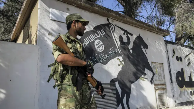 叙利亚一名反政府武装分子站在“伊斯兰国”标志前