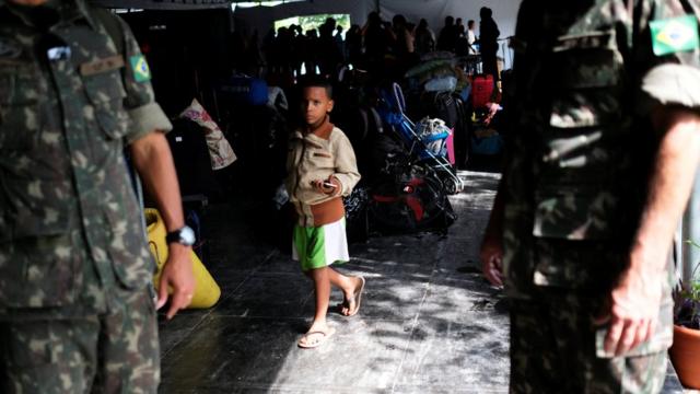 Militares em frente a garoto venezuelano esperando sua família mostrar passaporte ou identidade no controle fronteiriço de Pacaraima, em Roraima