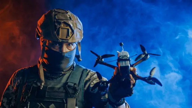 Солдат у бойовому спорядженні тримає дрон на тлі червоно-синього диму, що створює відчуття напруги та військових дій - стокове фото