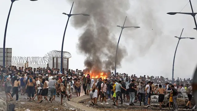 Cientos de personas que cruzaron la frontera se congregan alrededor de una estructura que fue incendiada en el enclave español de Ceuta, en el norte de África.