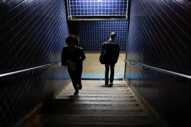 Mulher e homem andandoresenha esportes da sorteescada que dá acesso ao metrôresenha esportes da sorteSP