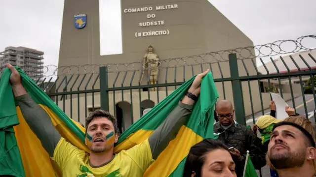 Pessoas de verde amarelo e com bandeiras do Brasil em frente a prédio com fachada: Comando Militar do Sudeste (II Exército)