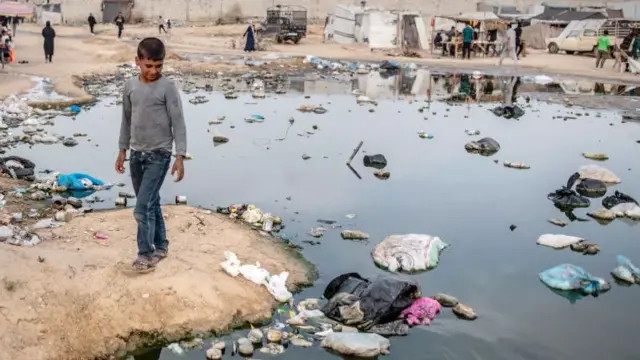 Un garçon palestinien marche près d'une piscine d'eaux usées avec des déchets à l'intérieur, à Rafah, le 26 avril 2024.