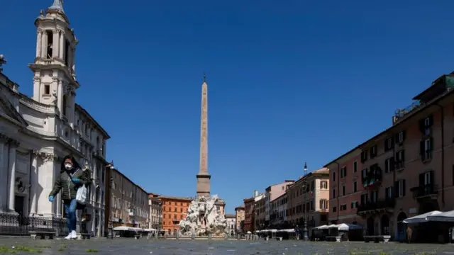 Mulher com máscara sobre a boca e o nariz caminhajogos de graça para jogaruma praça italiana completamente vazia a não ser por ela sob um céu azul sem nuvens