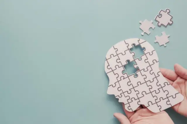 En la esquina inferior derecha, dos manos sostienen un puzzle que tiene la forma de una cabeza y a la que le faltan aún dos piezas por poner. 