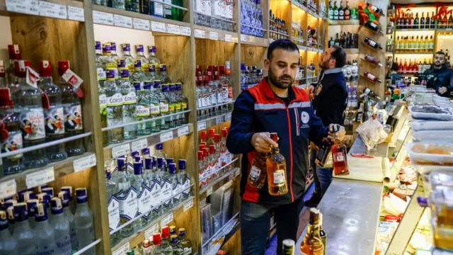 مسؤولون بينهم ضباط أمن خلال تفقدهم متجراً يبيع زجاجات خمر في تركيا خلال البحث عن مشروبات كحولية مقلدة