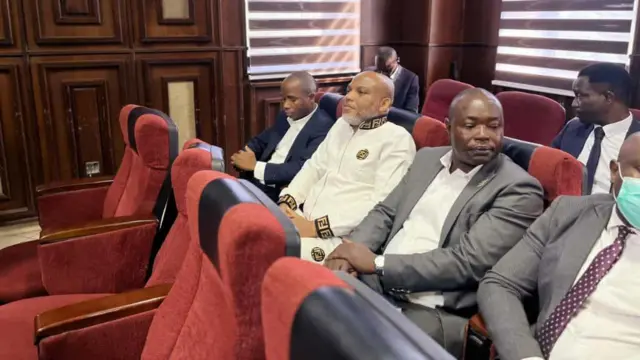 Nnamdi Kanu n'ọdụ n'oche n'ime ụlọikpe, n'etiti ndị ụlọọrụ DSS kpọtara ya maka ikpe ya.