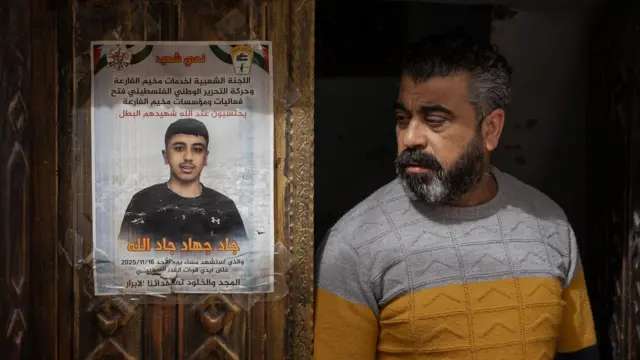 Jad'ın babası, işgal altındaki Batı Şeria'da bulunan El-Far'a mülteci kampındaki evin oyma ahşap ön kapısına yapıştırılmış, oğlunun anısına yapılmış bir posterin yanında duruyor.