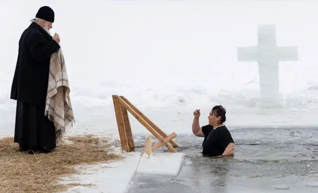 Жена излази из ледене воде језера док свештеник стоји у близини током прославе православног хришц́анског празника Богојављања у граду Ступино у Московској области.
